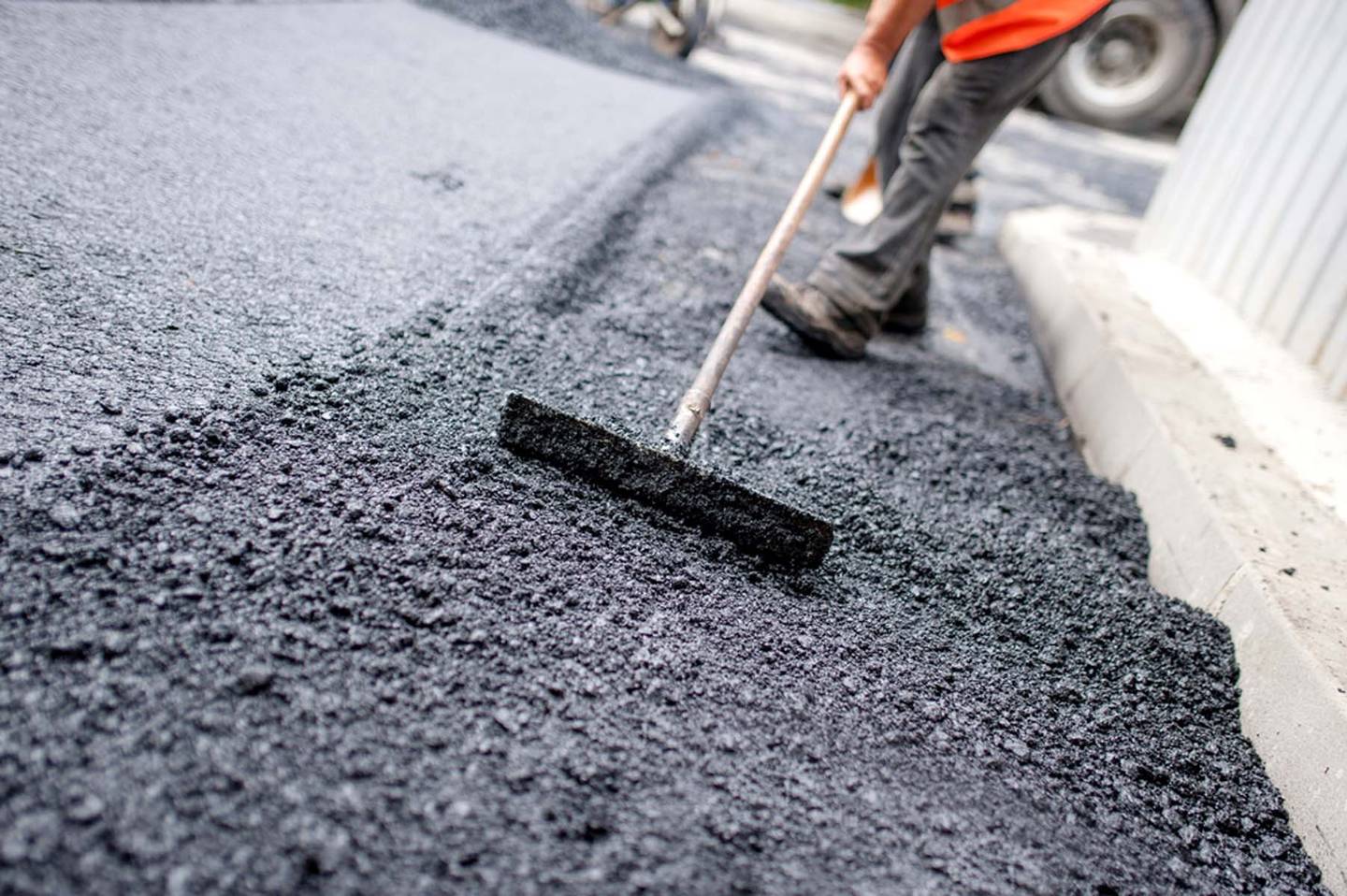 Crew member leveling a fresh mat of hot asphalt with a hand rake