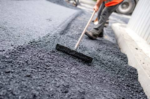 Crew member leveling a fresh mat of hot asphalt with a hand rake