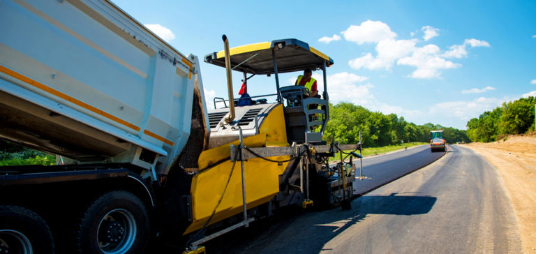 A paver laying a fresh mat of asphalt behind a delivery truck