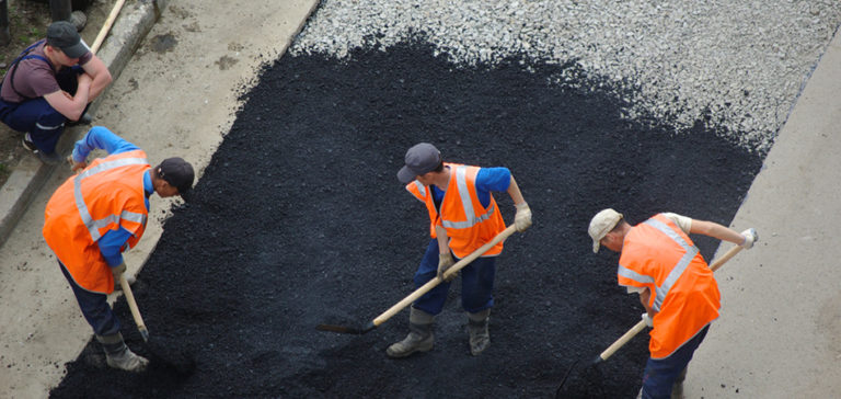 A crew working new asphalt across a stripped and prepared area