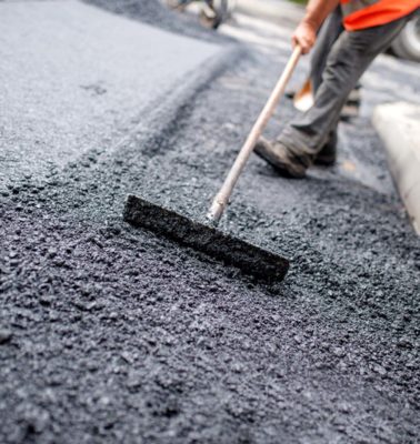 Worker leveling fresh asphalt on a road construction site, industrial buildings and teamwork - Turnkey Asphalt