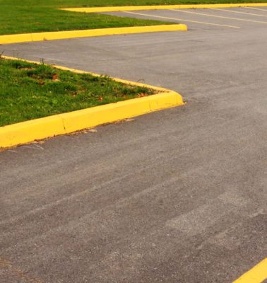 An empty, paved parking lot with yellow lines and curbs borders a grass landscape - Turnkey Asphalt