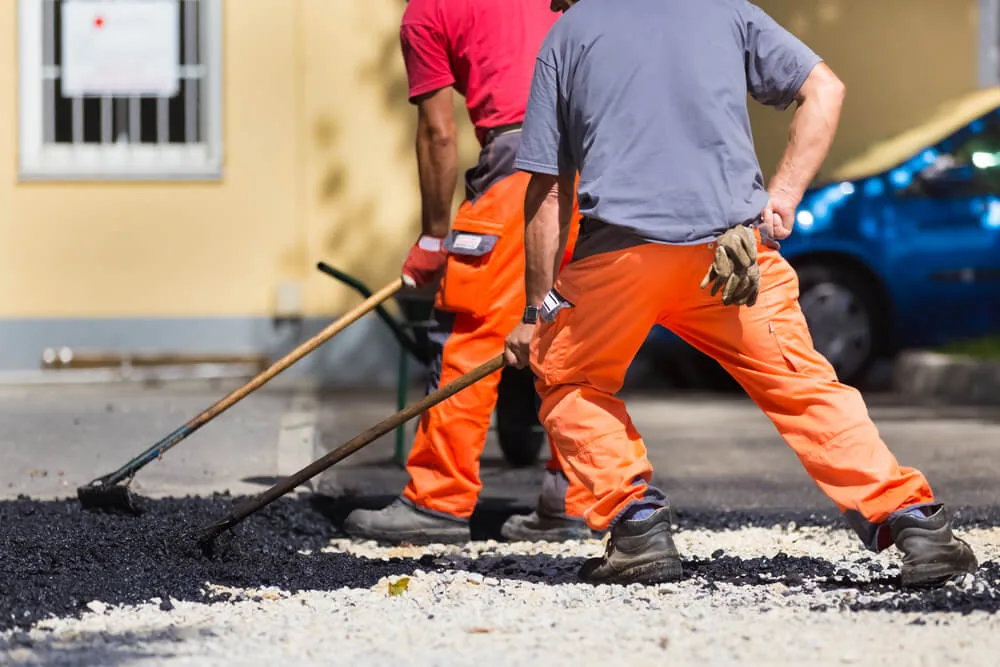 A crew raking hot asphalt into a patched area