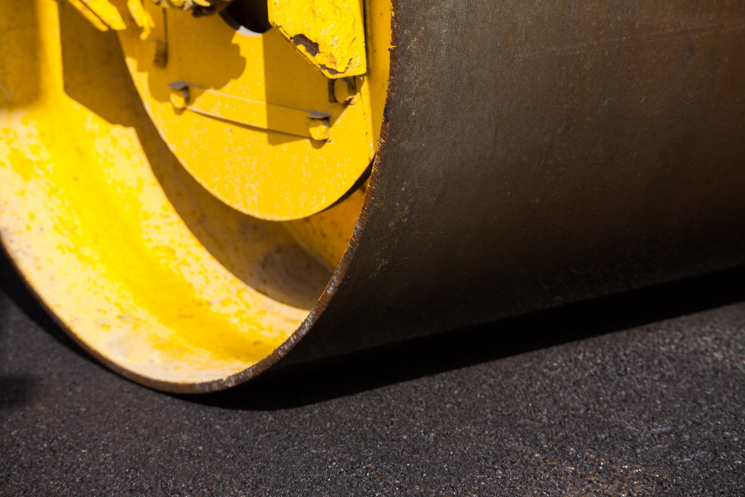 A roller drum pressing down a fresh asphalt mat