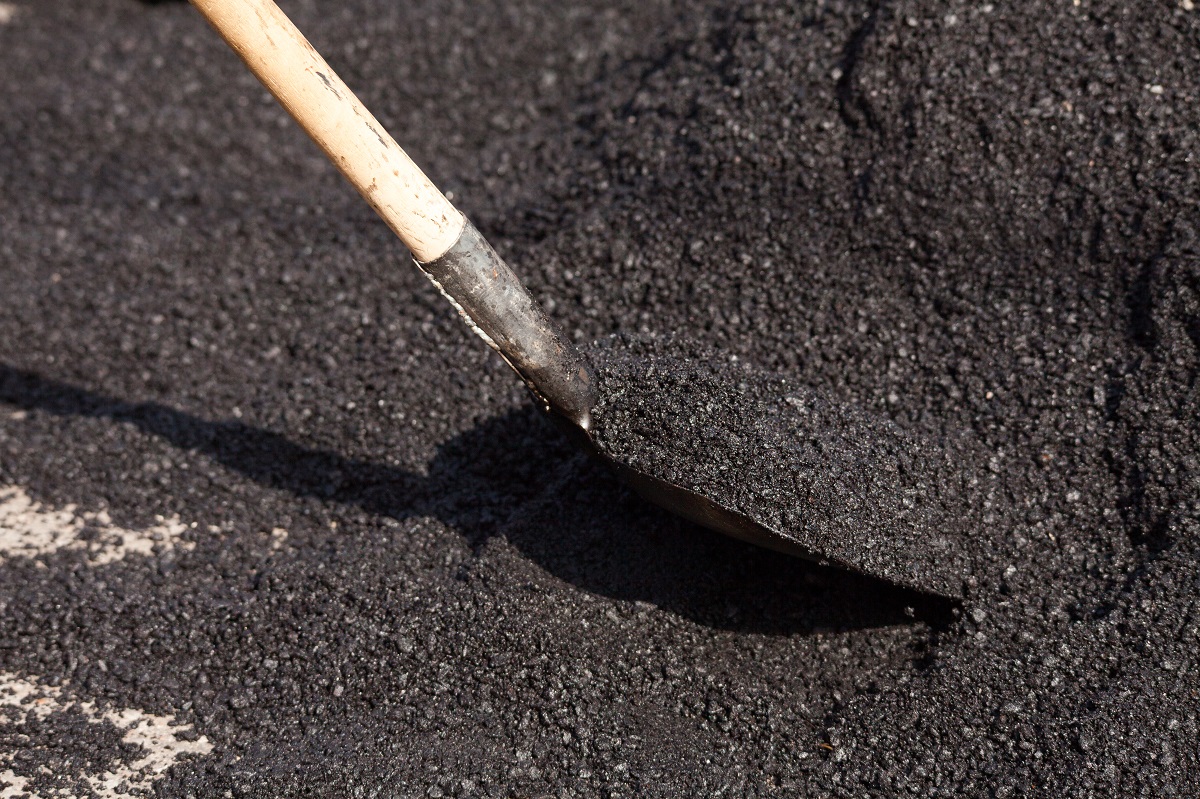 A rake lifting fresh hot asphalt on a new surface