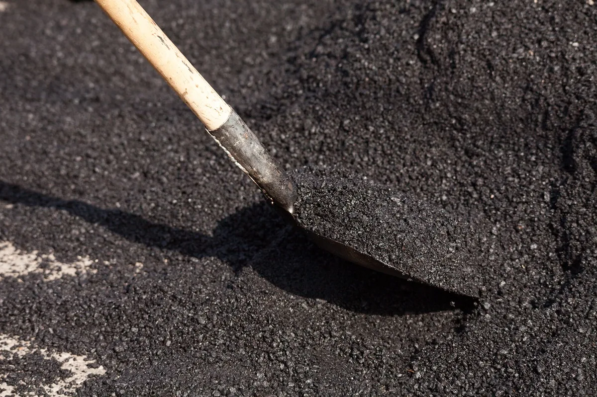 A rake lifting fresh hot asphalt on a new surface