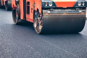 Heavy machines work diligently on a city street, laying fresh asphalt. The bright sun shines down as crews upgrade the road surface, ensuring smooth travel for vehicles and pedestrians alike.