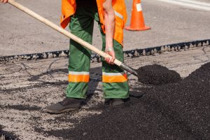 Workers on Asphalting paver machine during Road street repairing works. Street resurfacing. Fresh asphalt construction. Bad road