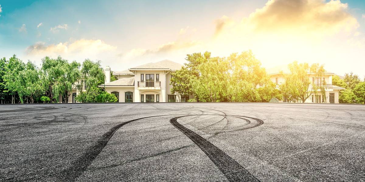 A wide asphalt lot with tyre marks, in front of a residential property
