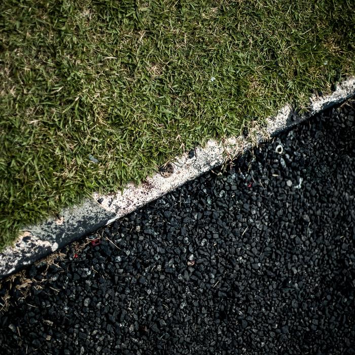 The clean edge of a newly laid asphalt surface against turf