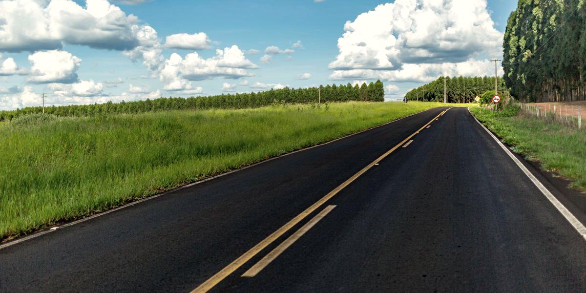 A finished asphalt road running straight between open fields