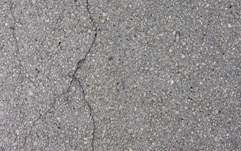 A crack running through an asphalt surface, with the aggregate visible around it