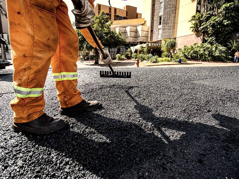 Asphalt patch material being raked level by hand over a repaired crack