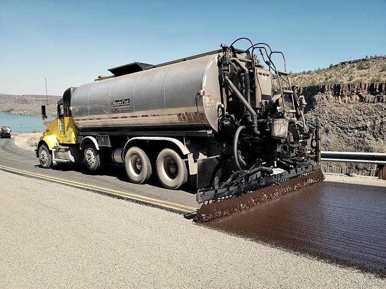 Asphalt distributor laying a fresh black surface across a road