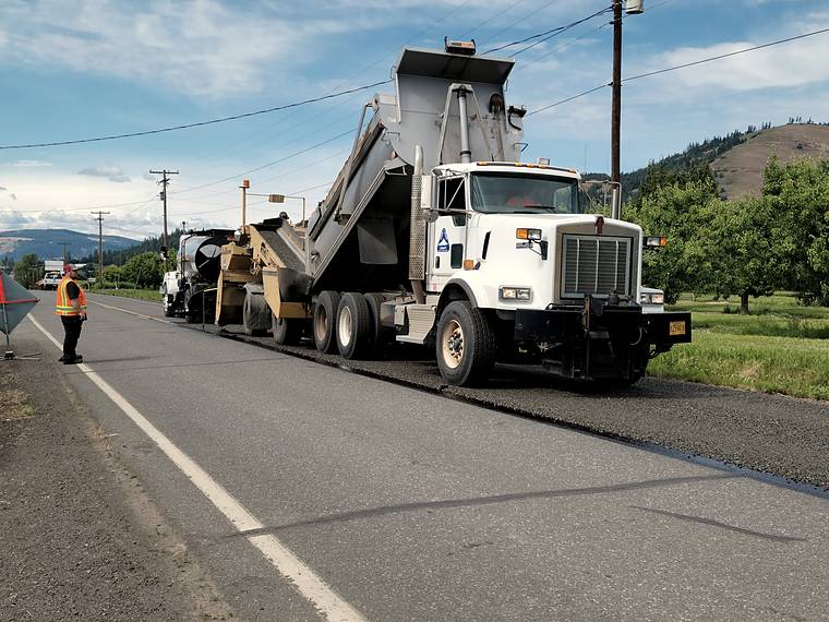 Paving crew finishing a fresh asphalt surface behind a dump truck