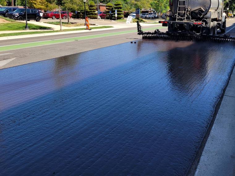 A distributor truck laying fresh sealer across a street